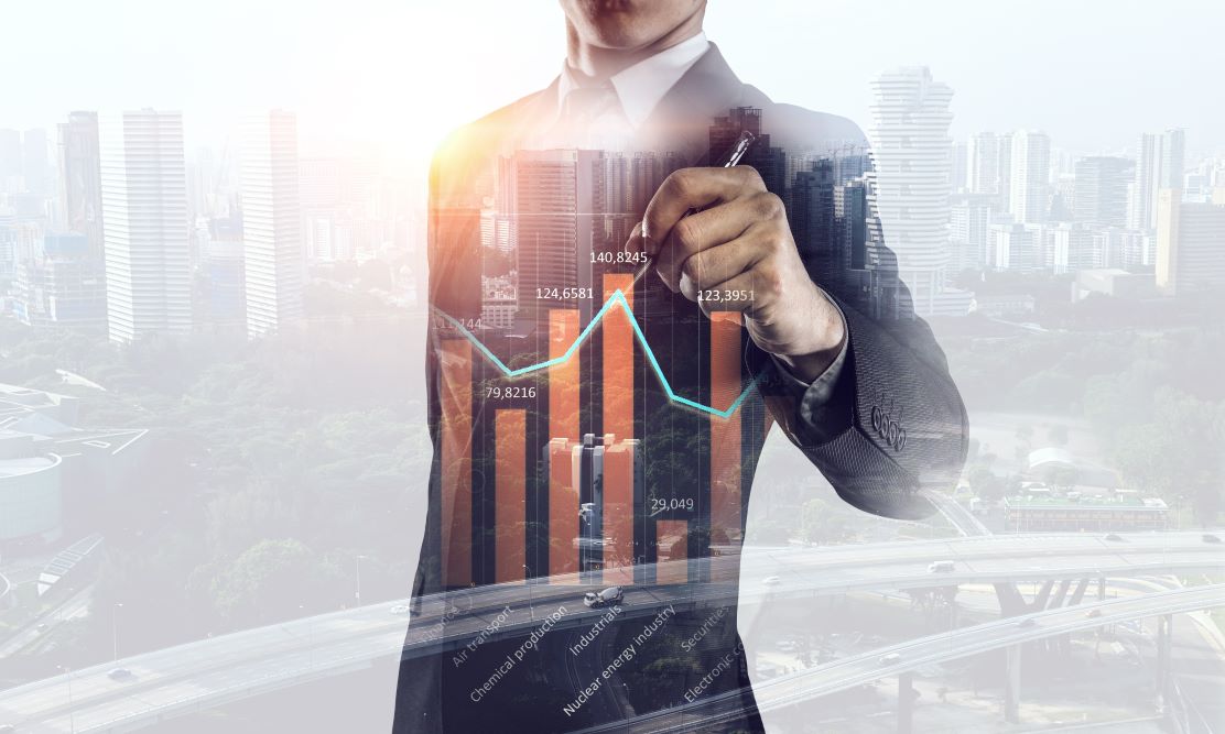 An abstract photograph of a professional using a pen to point to a bar graph, overlayed onto a city skyline at dawn.